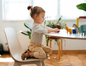 a girl sits on a chair, interested in toys on the table in front of her