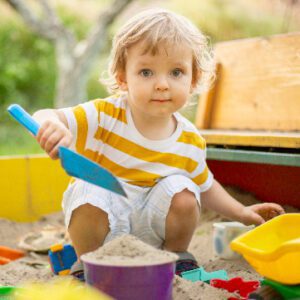 a toddler-age boy plays in a sandbox
