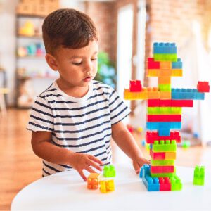 a boy stacks building blocks in a sunny room
