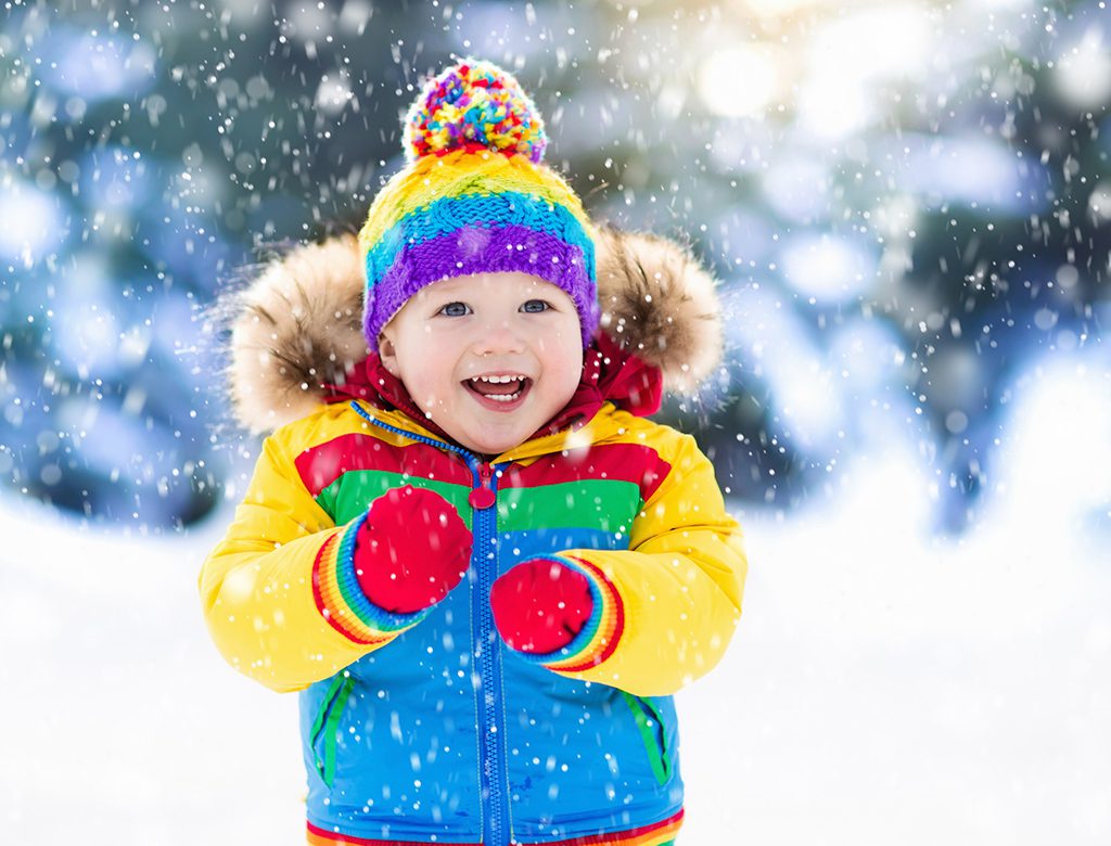 Young child wearing colorful clothes laughing in the snow